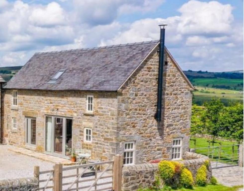 uma casa de pedra com uma cerca em frente em Cuckoostone Barn em Buxton