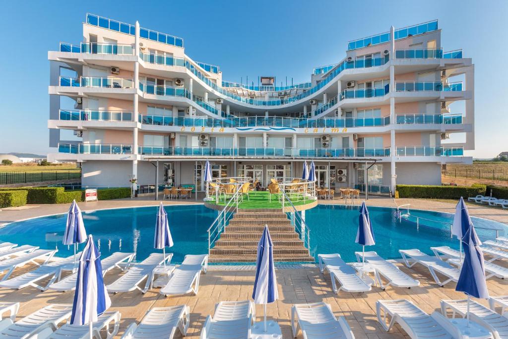 een hotel met stoelen en een zwembad en een gebouw bij Aparthotel Costa Calma in Aheloy