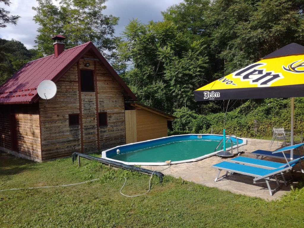 a swimming pool next to a house with an umbrella at Alaske kolibe in Bajina Bašta