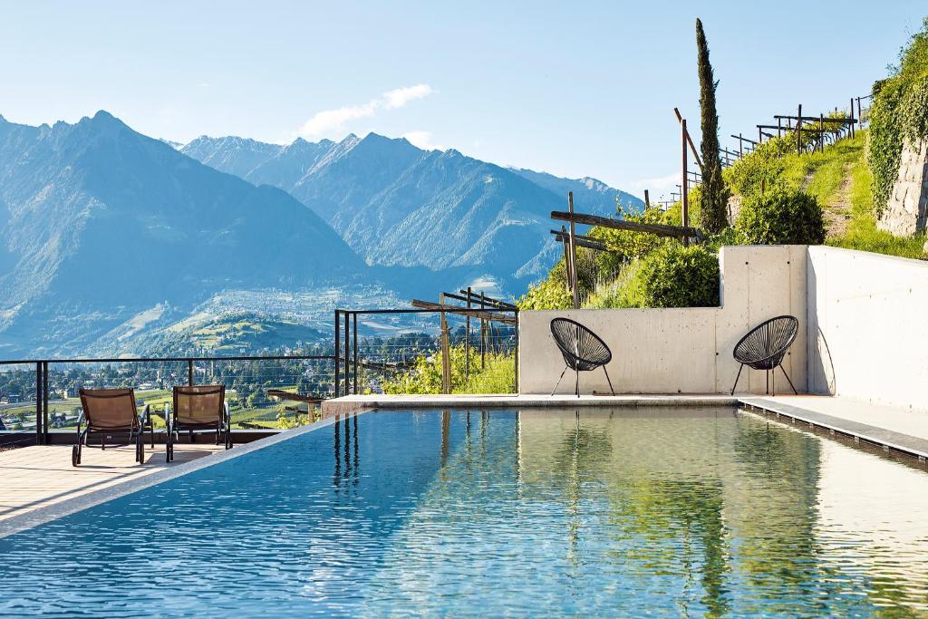 a swimming pool with chairs and mountains in the background at Pratenberg Wine Lodge in Merano