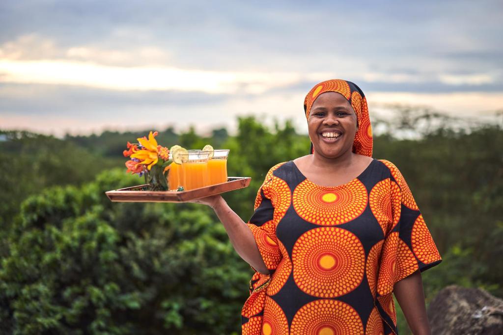 een vrouw met een dienblad met drankjes en bloemen bij Hillside Retreat – Africa Amini Life in Usa River