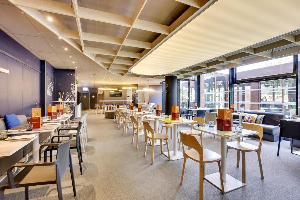a restaurant with tables and chairs and windows at ibis Styles Paris Charles de Gaulle Airport in Roissy-en-France