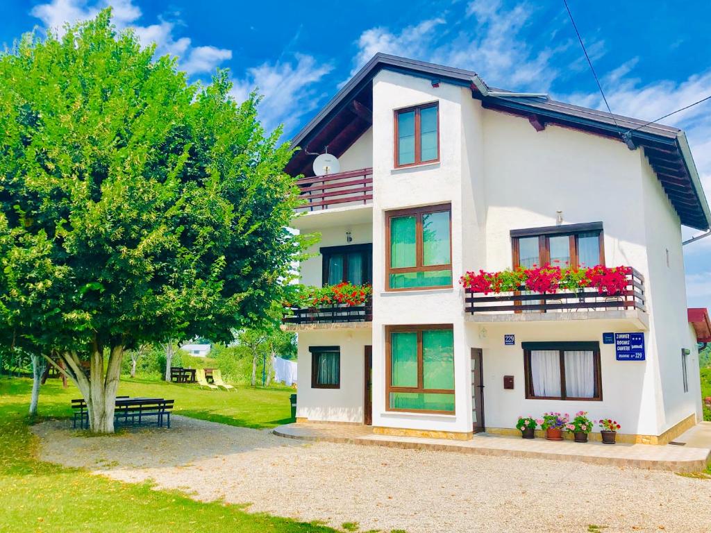 Biały dom z kwiatami na balkonach i drzewem w obiekcie House Turkalj w mieście Grabovac