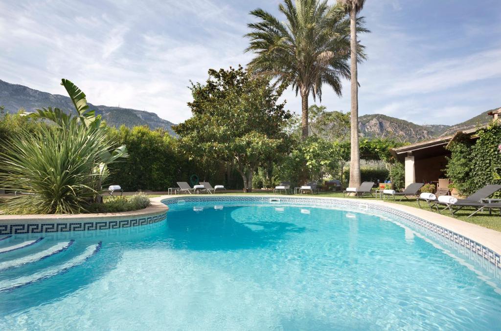 a large swimming pool with palm trees and mountains at Finca Ca'n Quatre in Sóller