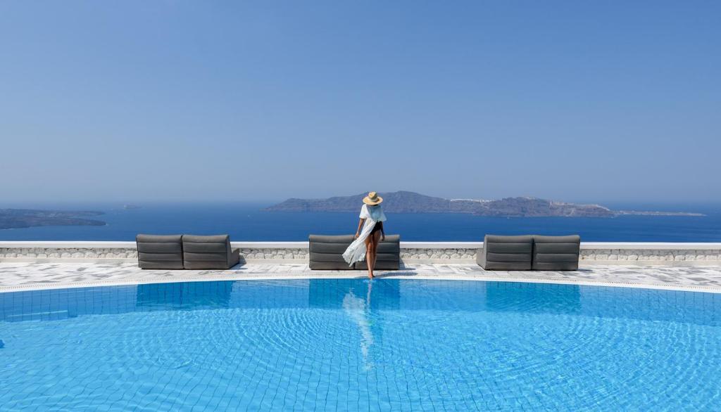a woman sitting on a chair next to a swimming pool at Xenones Filotera in Imerovigli