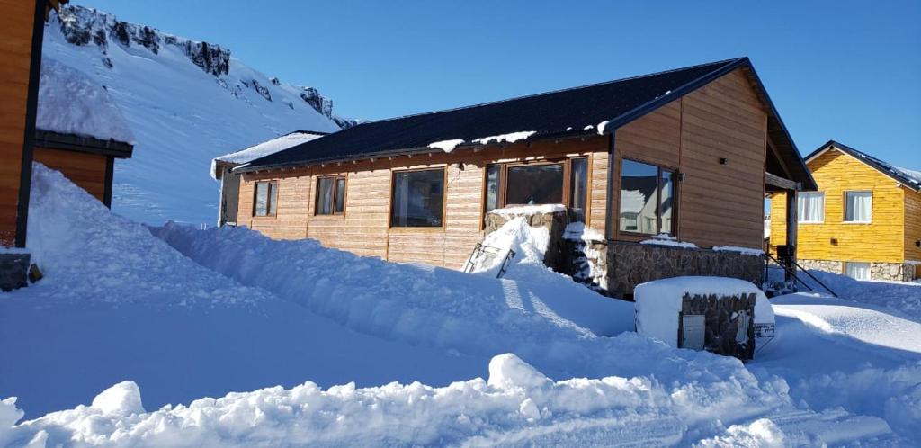 una casa cubierta de nieve junto a un montón de nieve en PEWMA Casa de Montaña en Caviahue