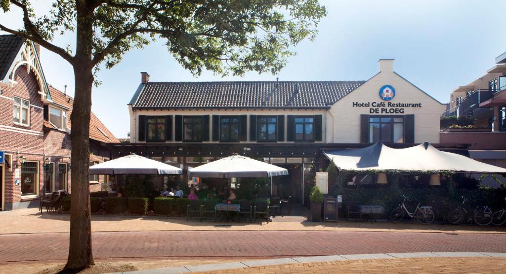a building with tables and umbrellas in front of it at Hotel Café Restaurant De Ploeg in Varsseveld