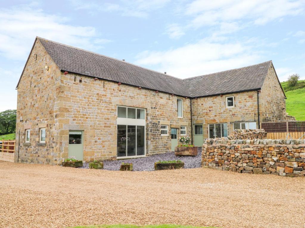 a large brick building with a stone wall at Pastures Barn in Leek
