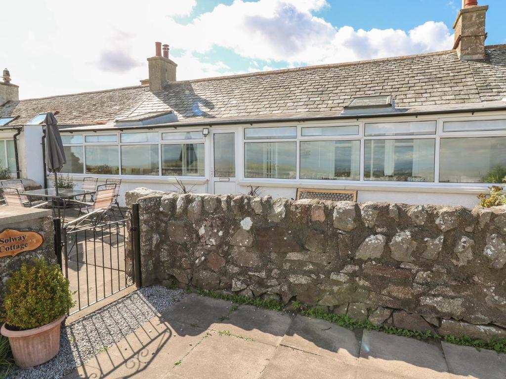 a house with a stone wall and a fence at Solway Cottage in Dumfries