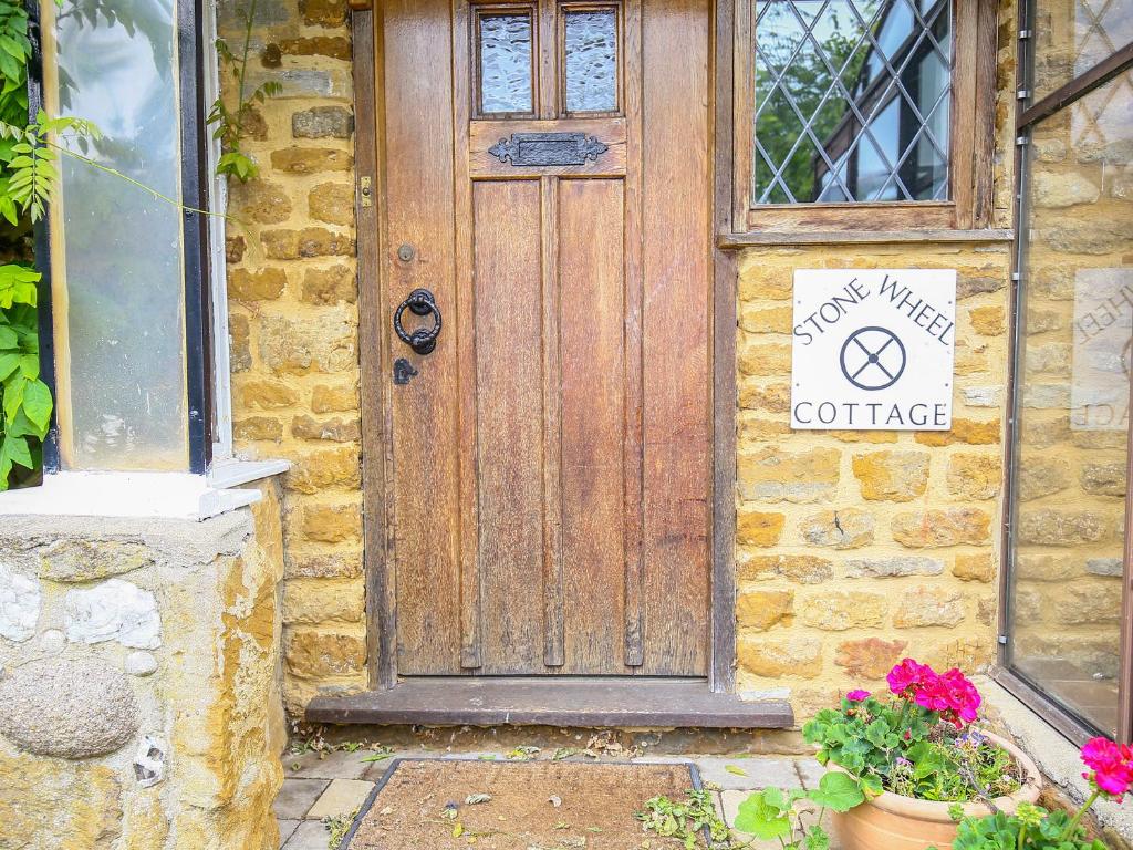 een houten deur op een stenen gebouw met een bord erop bij Stone Wheel Cottage in Hook Norton