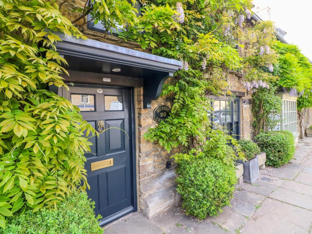 a blue door on a brick building with plants at Murton Cottage in Burford