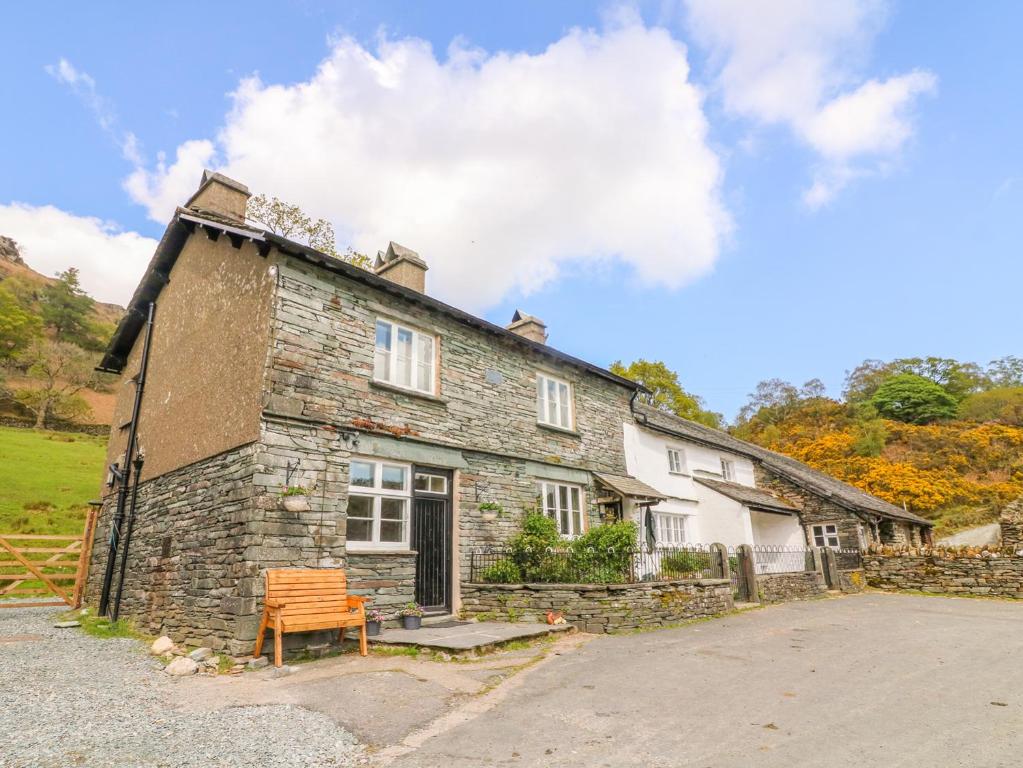 ein altes Steinhaus mit einer Bank davor in der Unterkunft Tilberthwaite Farm Cottage in Coniston
