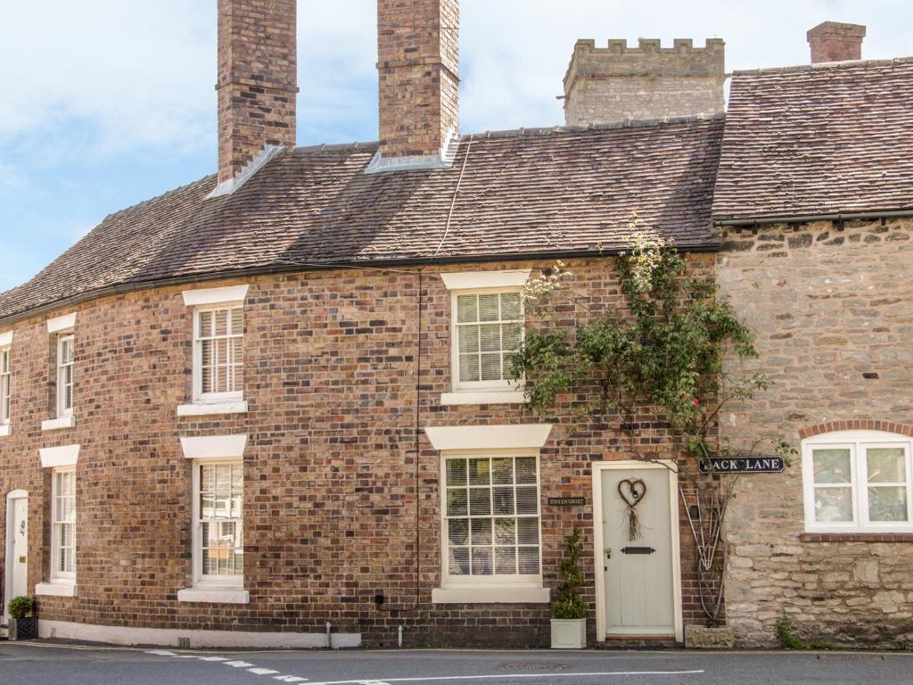 ein altes Backsteinhaus mit weißer Tür in der Unterkunft Queens Cottage in Much Wenlock