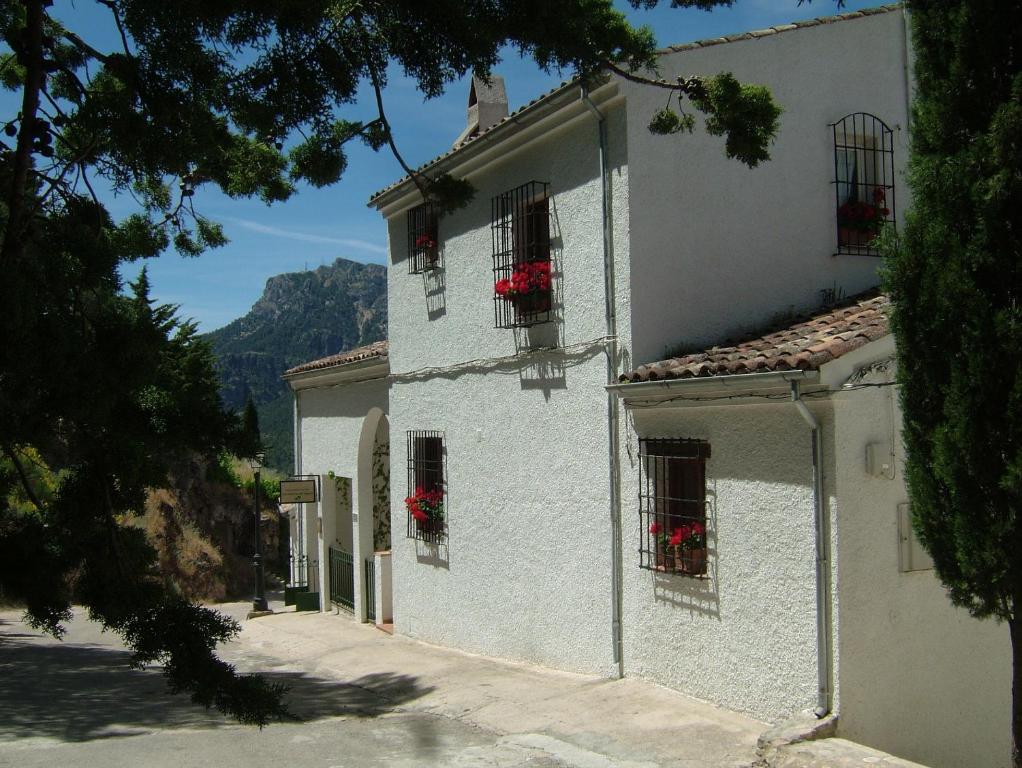 een wit gebouw met rode bloemen in de ramen bij Los Huertos de Segura in Segura de la Sierra