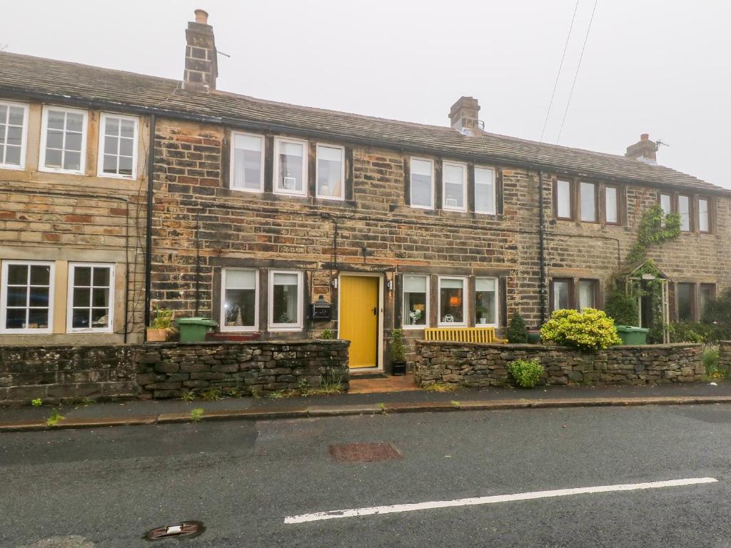 a brick building with a yellow door on a street at Fleece Cottage in Holmfirth