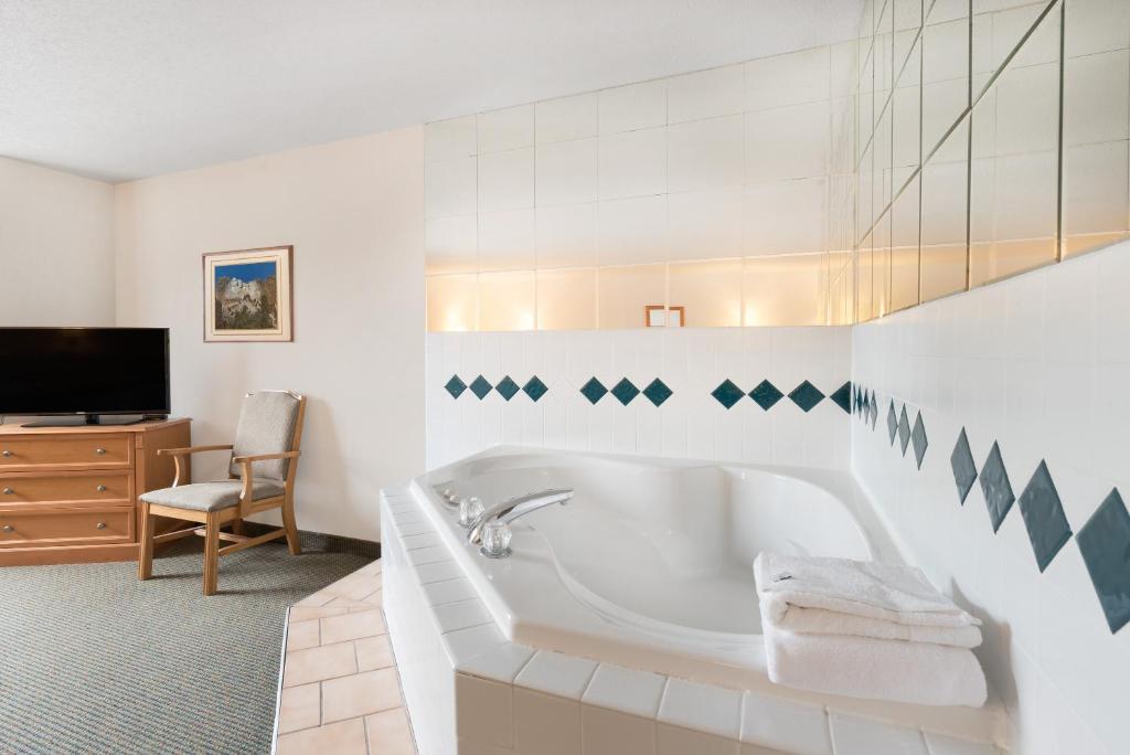 ein weißes Bad mit einer Badewanne und einem TV in der Unterkunft Baymont by Wyndham Hot Springs in Hot Springs