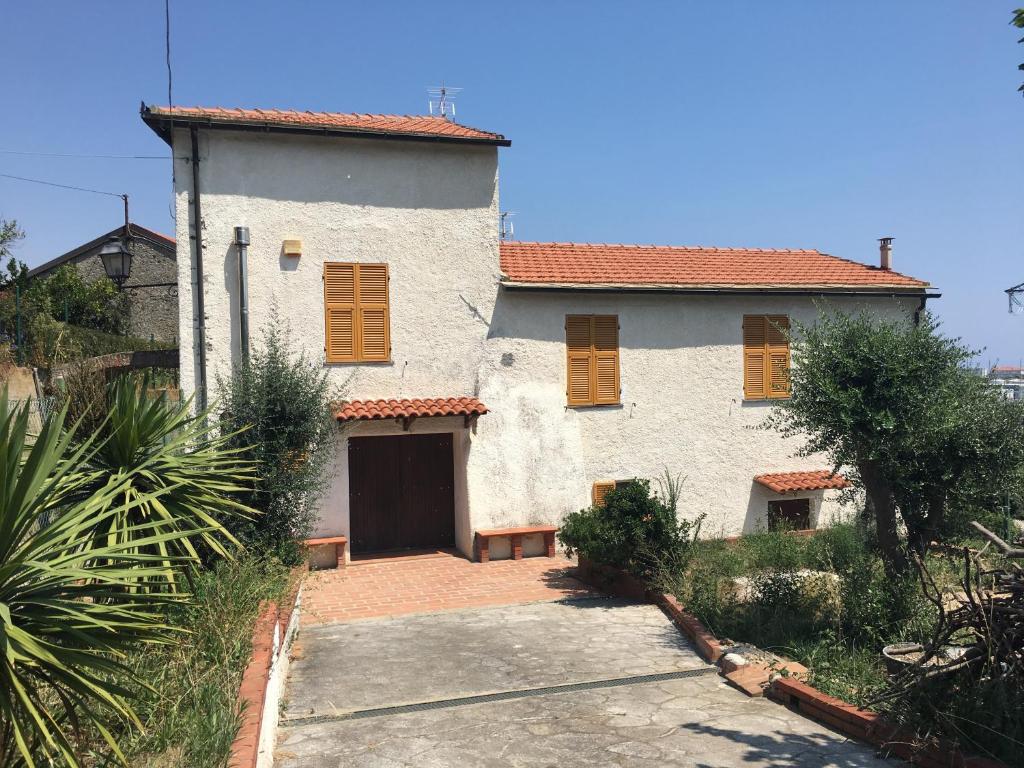 a white house with orange shuttered windows and a driveway at In campagna al mare in Quiliano