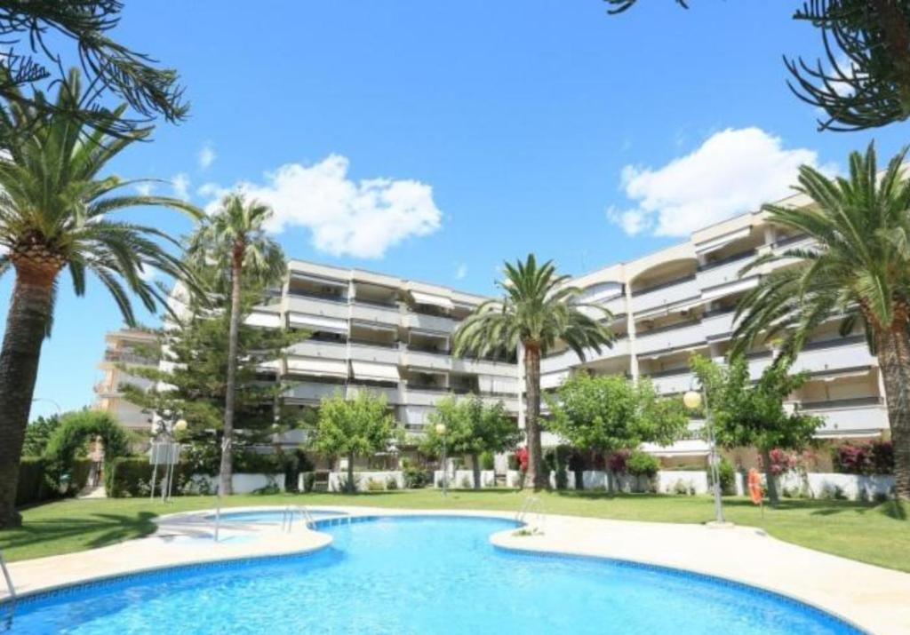 una piscina frente a un edificio con palmeras en Cambrils Regata Apartamento junto el mar en Cambrils