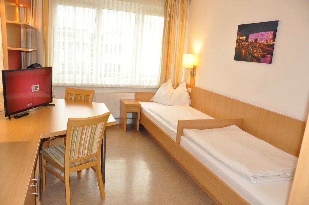 a room with two beds and a desk and a television at Kolpinghaus Linz in Linz