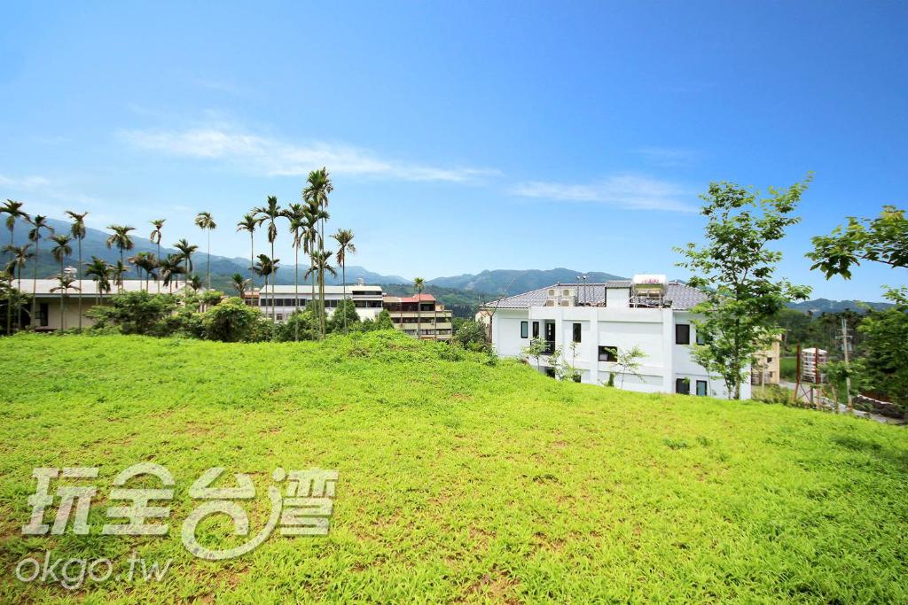 a green hill with buildings and palm trees on it at Do Tian Ding B&B in Lugu