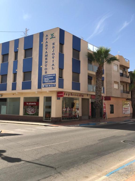 a building on a street with a palm tree in front of it at APARTAMENTOS ESJOVIAL in Los Alcázares