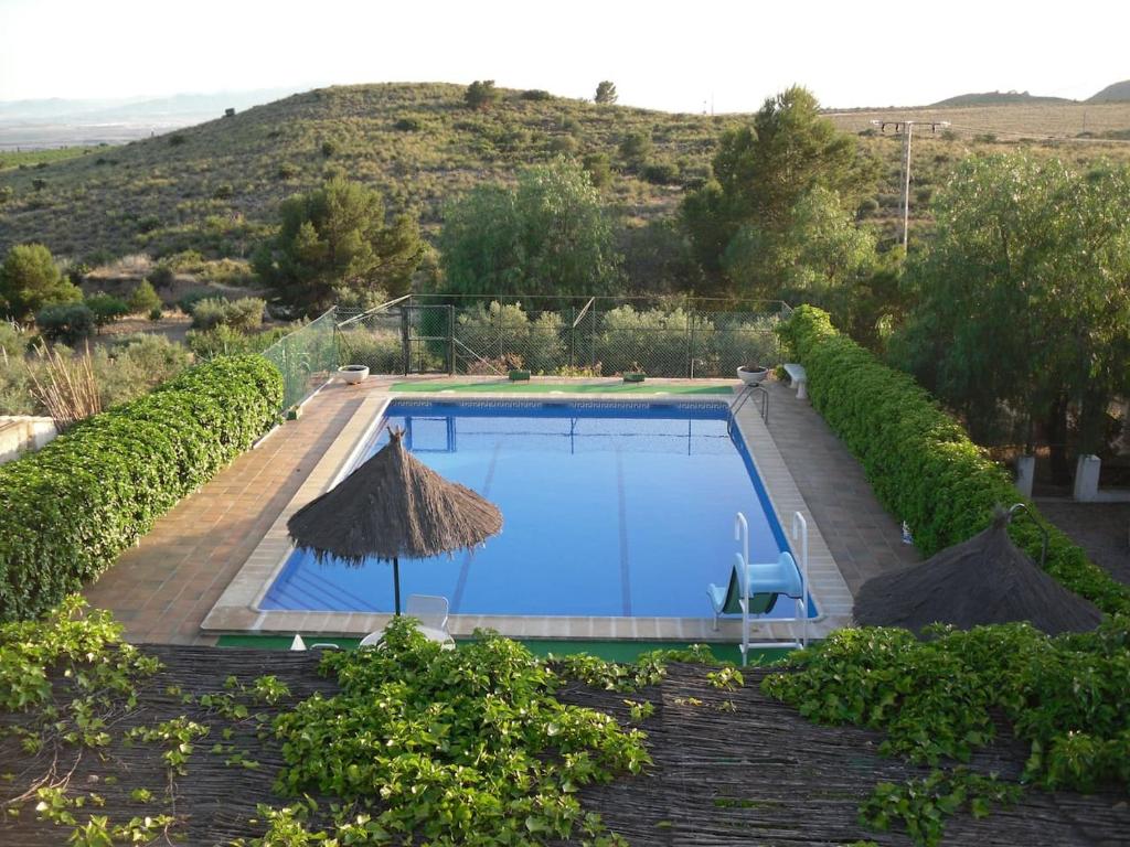 uma piscina com um guarda-sol de palha e um resort em Chalet rural en la Sierra de Carrascoy em Almagros
