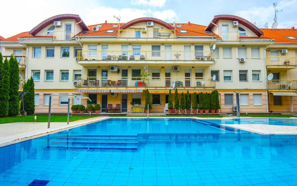 a swimming pool in front of a large building at Kis-Gast Panoráma Apartman in Hajdúszoboszló