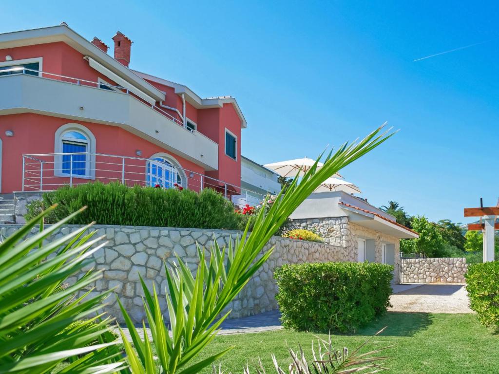 a red house with a stone wall and a palm tree at Apartment Jadranka-2 by Interhome in Rab