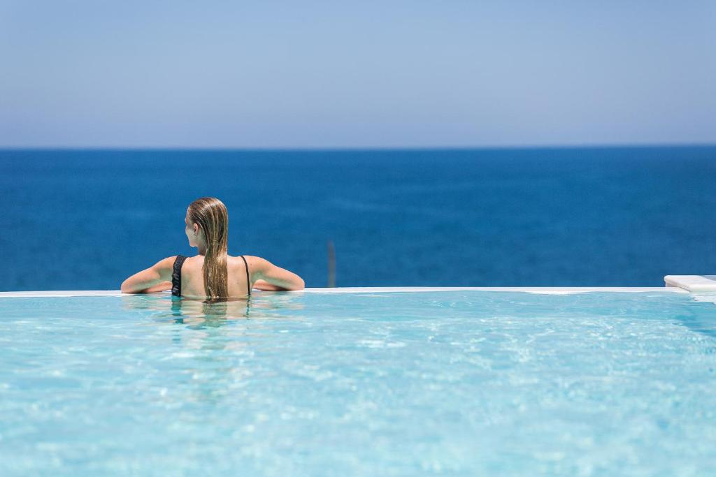 una mujer sentada en una piscina con vistas al océano en Wave Villa, Seaside Living & Your Own Beach Spot, By ThinkVilla, en Panormos Rethymno