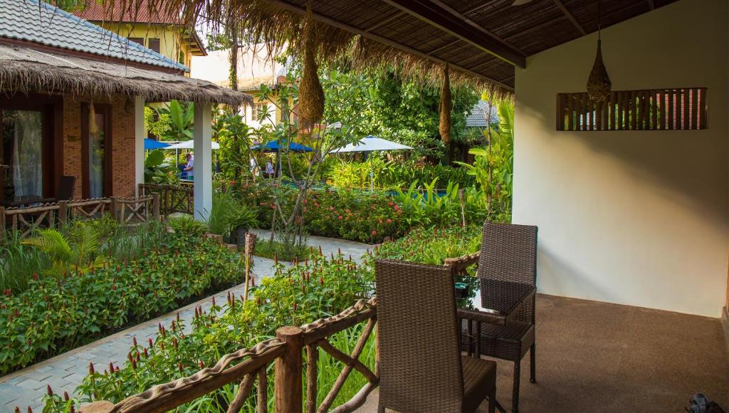 a patio with two chairs and a table in a garden at La Rivière d' Angkor Resort in Siem Reap