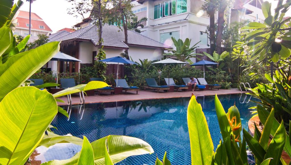 a swimming pool with chairs and umbrellas next to a building at La Rivière d' Angkor Resort in Siem Reap