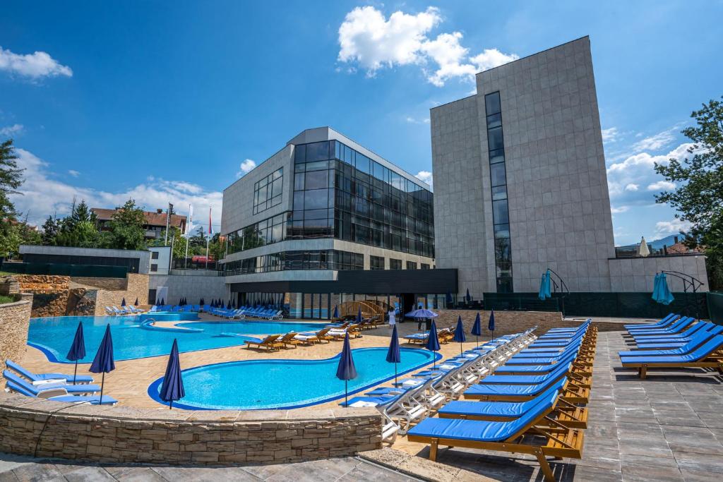 a pool with blue lounge chairs and a building at Hotel Tonanti in Vrnjačka Banja