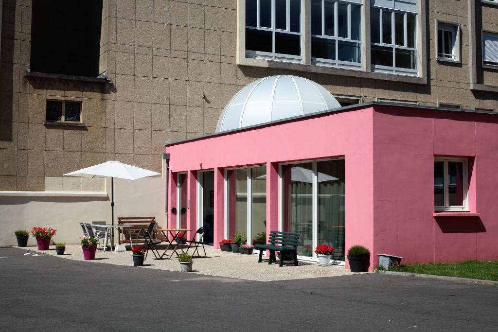 een roze gebouw met een tafel en een paraplu bij Résidence La Providence ZENAO Lisieux in Lisieux