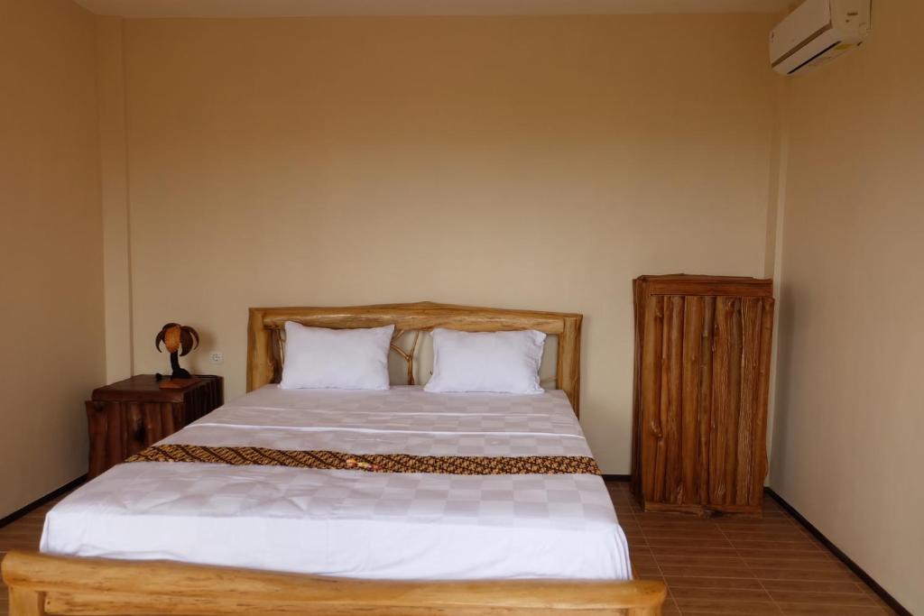 a bedroom with a bed with white sheets and wooden furniture at Kelapa Surf Villa in Jembrana