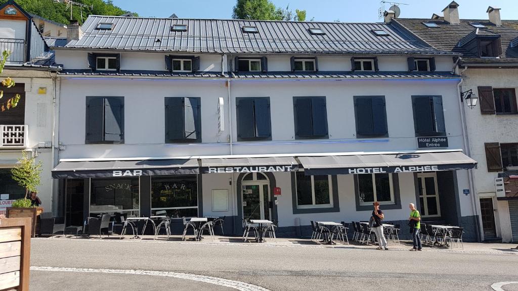 a white building with tables and chairs on a street at Hôtel Alphée in Barèges