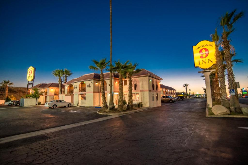 a city street with a yellow motel sign and palm trees at National 9 Inn in Buttonwillow