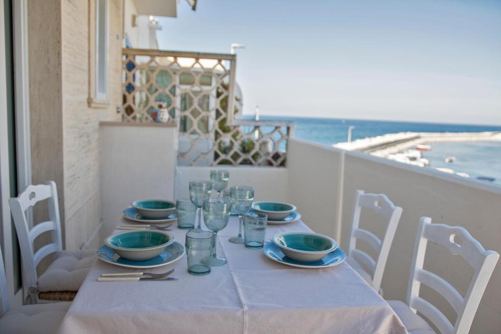 una mesa con platos y vasos en un balcón con vistas al océano en Il mare di fronte “Casa Smeraldo”, en Savelletri di Fasano