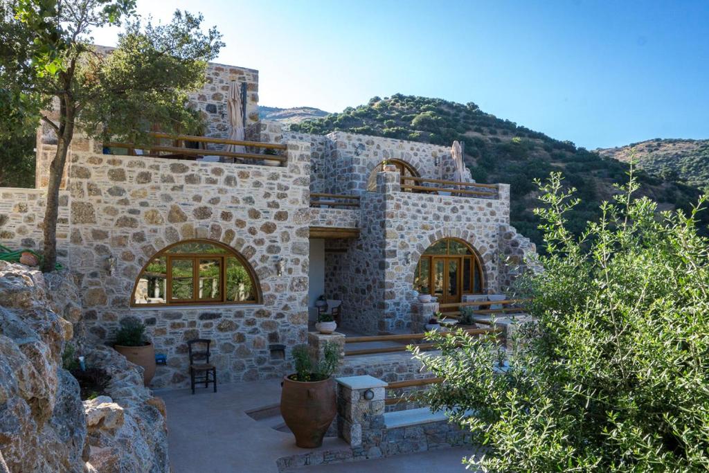 a stone house with a patio with trees and mountains at To Spiti mas in Sougia