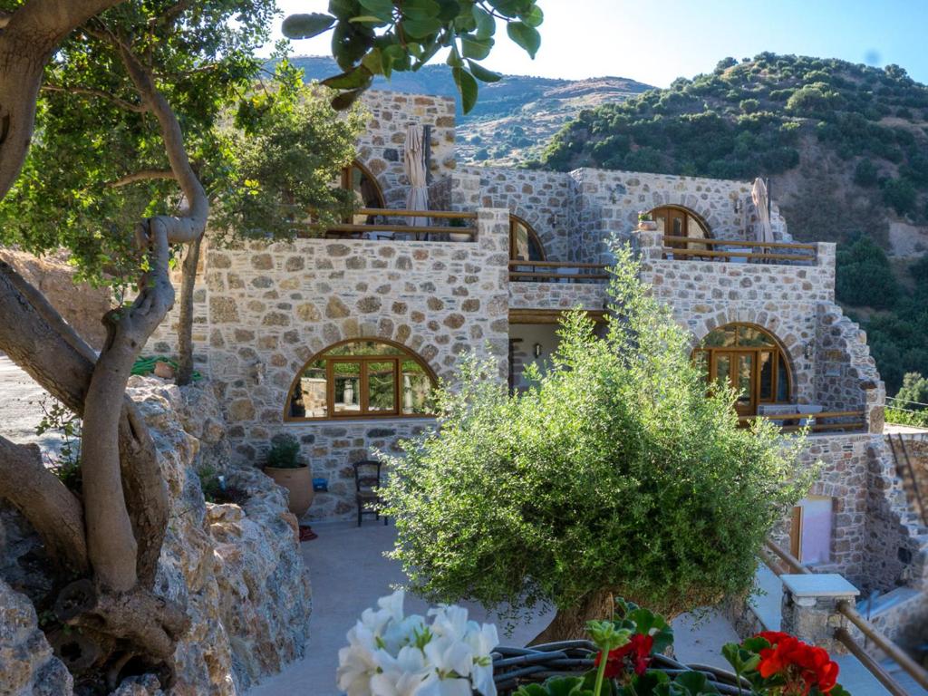 una casa de piedra con árboles y flores delante de ella en To Spiti mas, en Sougia
