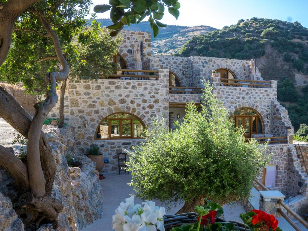 a stone house with trees and flowers in front of it at To Spiti mas in Sougia