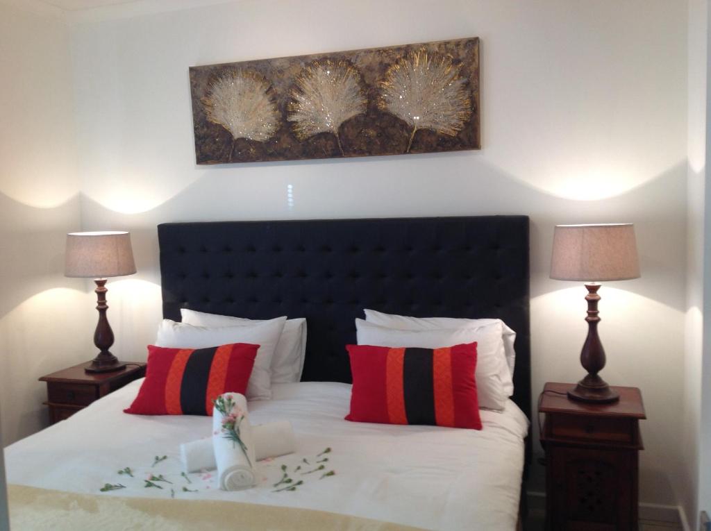 a bedroom with a bed with red and black pillows at Secret Garden Guesthouse in Bloubergstrand