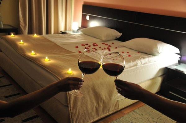 two people holding wine glasses in front of a bed at Hotel Beograd - Yu in Sarajevo
