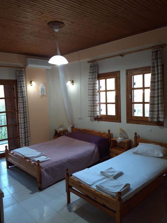 two beds in a bedroom with two windows at Koutadelias rooms in Kalamos
