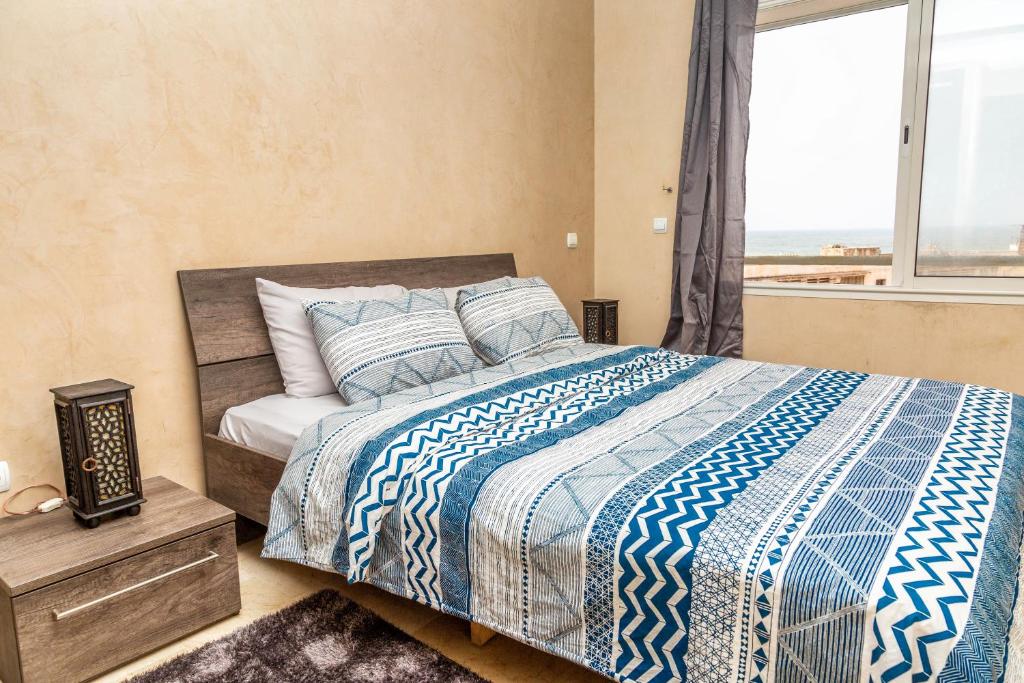 a bedroom with a bed with a blue and white comforter and a window at Appartement Panoramique in Casablanca