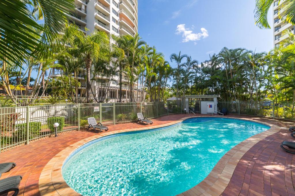 a swimming pool with two chairs and palm trees at The Meriton Apartments on Main Beach in Gold Coast