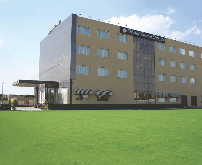 a large building with a green field in front of it at Hotel Grand Maple in Jaipur