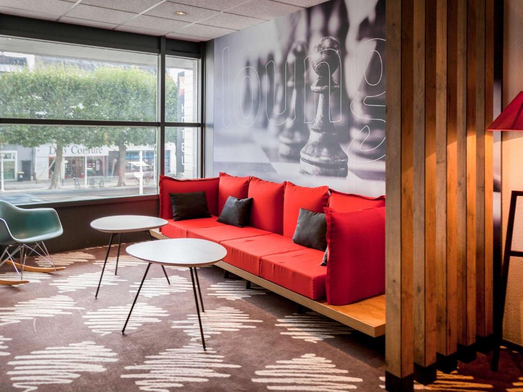 - un canapé rouge dans une chambre avec des tables et une fenêtre dans l'établissement ibis Lorient Centre Gare, à Lorient