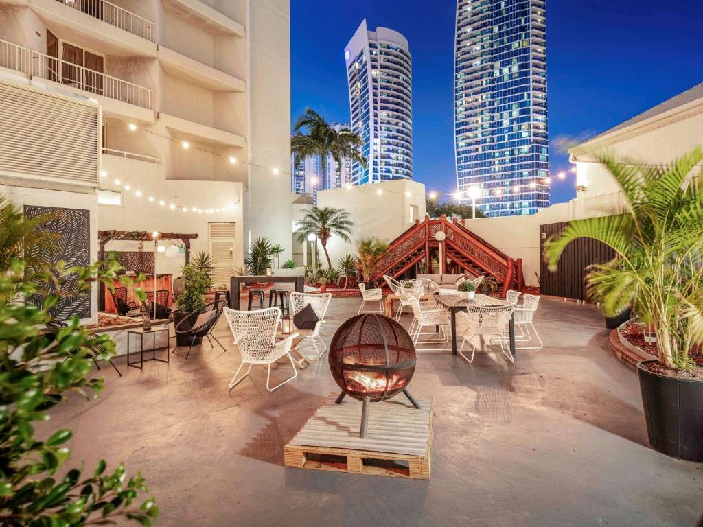 d'une terrasse avec des chaises blanches, des tables et des bâtiments. dans l'établissement Novotel Surfers Paradise, à Gold Coast