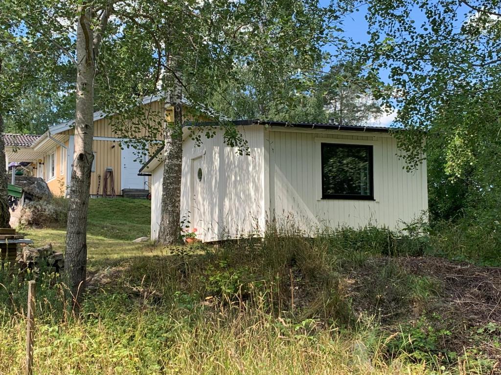 a small white house with a window and trees at The Little Swedish Stuga in Hölö