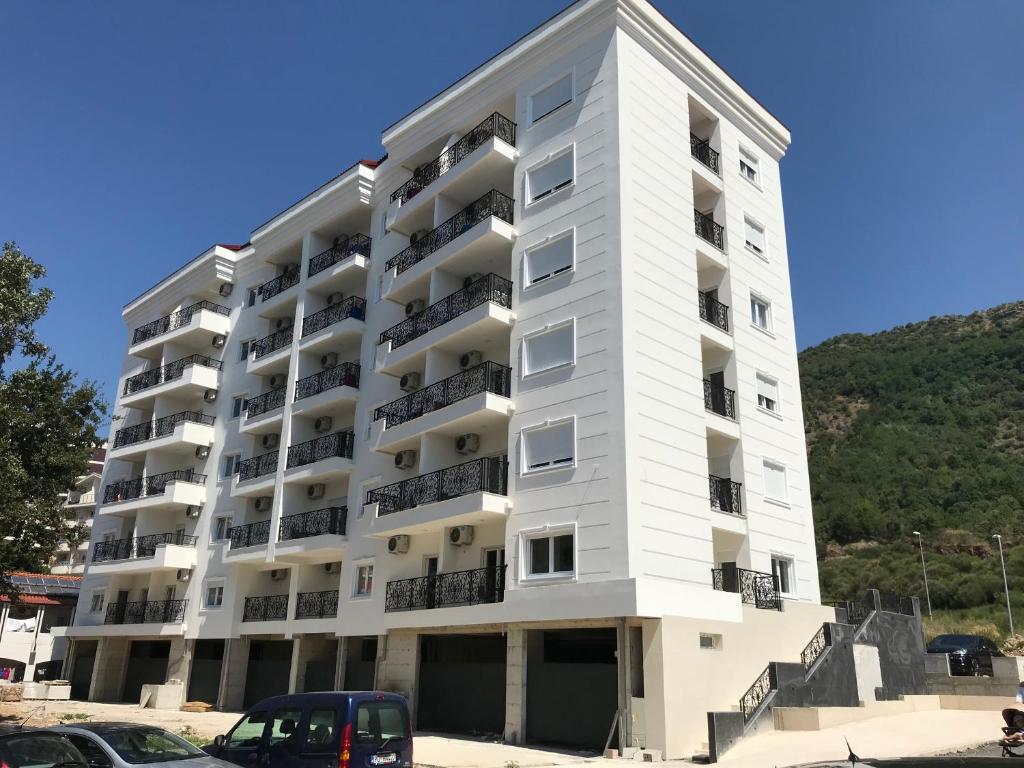 un edificio de apartamentos blanco con coches estacionados frente a él en APARTMENTS TOMIĆ, en Bečići